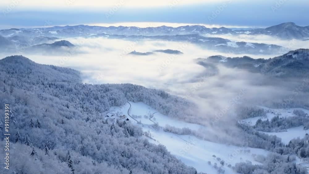 Aerial shot of Slovenia's snowy mountains and hills surrounded by fog Aerial shot of Slovenia's snowy mountains and hills surrounded by fog