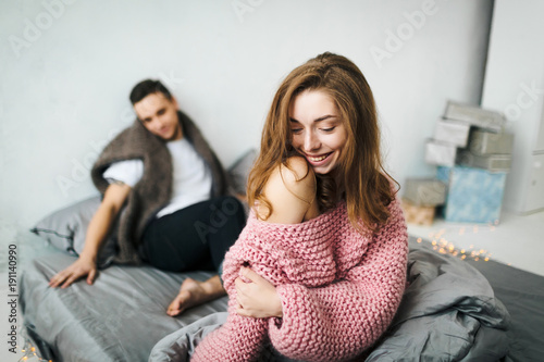 Happy couple sitting on a bed. The woman in the foreground and blurred man. Artwork