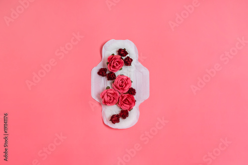 White sanitary pad with red and pink flowers on it, woman health or body positive concept. Pink background.  Flatlay. Copyspace photo