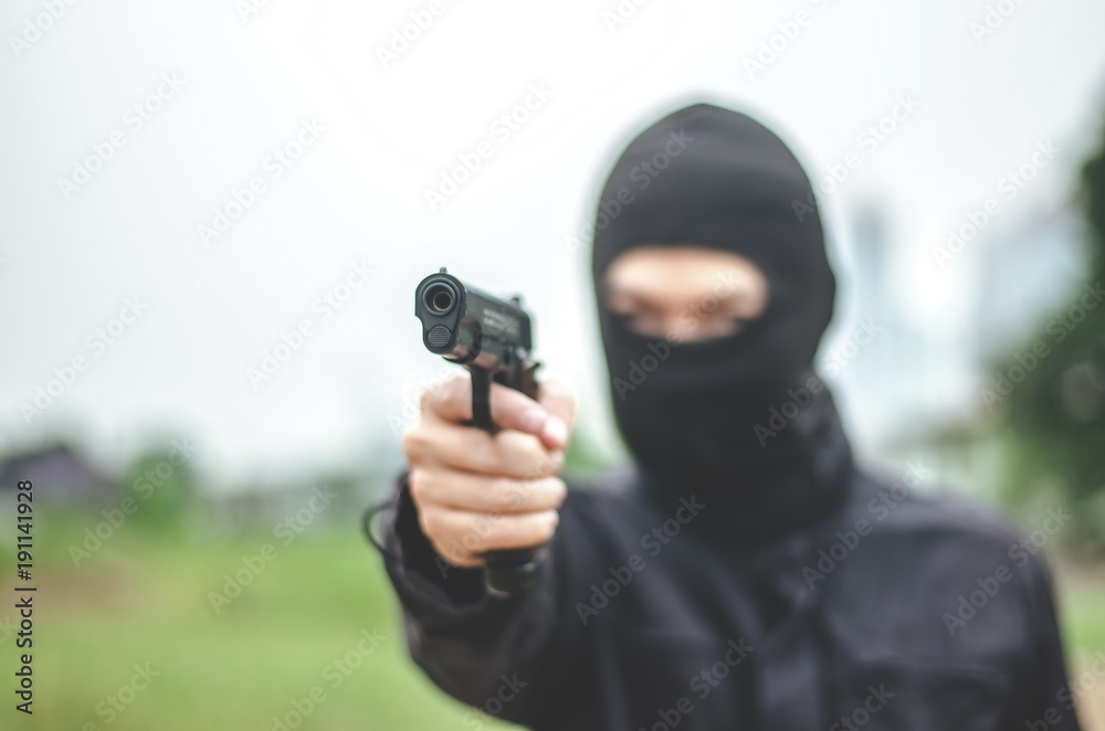 Mask thief in balaclava with holding gun ,Outlaw bad man hold a gun pointing the target , robber in black hood holding gun and pointing to victim Mask thief in balaclava with holding gun ,Outlaw bad man hold a gun pointing the target , robber in black hood holding gun and pointing to victim