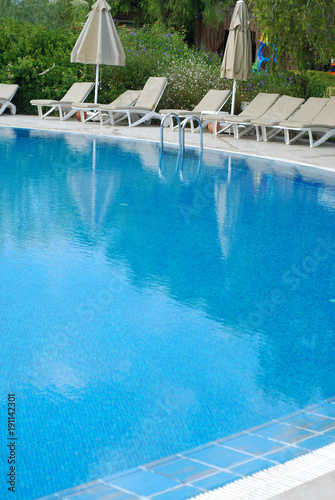 Sweeming Pool with Blue Water with Sun Umbrella and Seetings. Vertical Image. Summer and Vacation Concept.