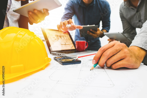 Three colleagues discussing data working and tablet, laptop with on on architectural project at construction site at desk in office 