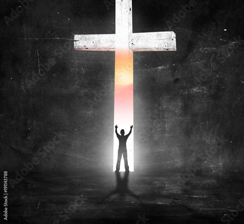Silhouette people raising hands over white cross on dark room background photo