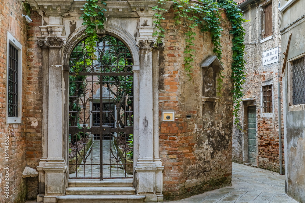 Fototapeta premium Old courtyard with ornate gate and narrow street in Venice Italy