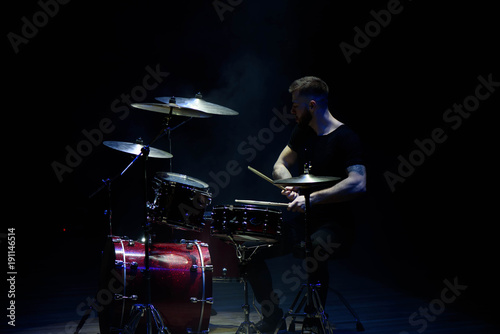 music, people, musical instruments and entertainment concept - male musician with drumsticks playing drums on the stage.