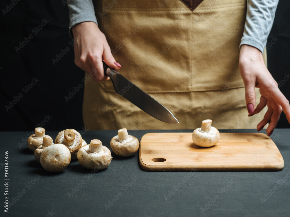 Woman cutting raw mushrooms on wooden board