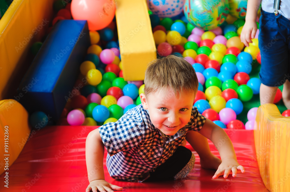 Obraz premium Boys playing on the playground, in the children's maze with balls. Multi-colored balls.