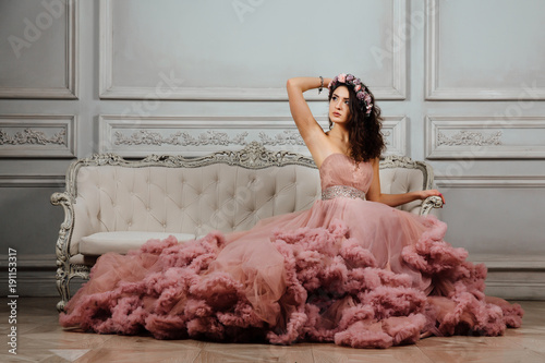 Luxurious sexy girl in an evening cloudy dress sitting on a sofa in the studio interior. photo