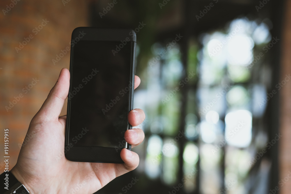 mockup image of hand holding smartphone in cafe restaurant. mobile phone with blank white screen in coffee shop.