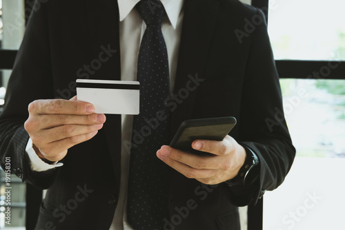 Fototapeta Naklejka Na Ścianę i Meble -  man holding a credit card and using smart phone for online shopping at cafe. businessman purchase goods from internet at office. male adult make payment on bank website at workplace
