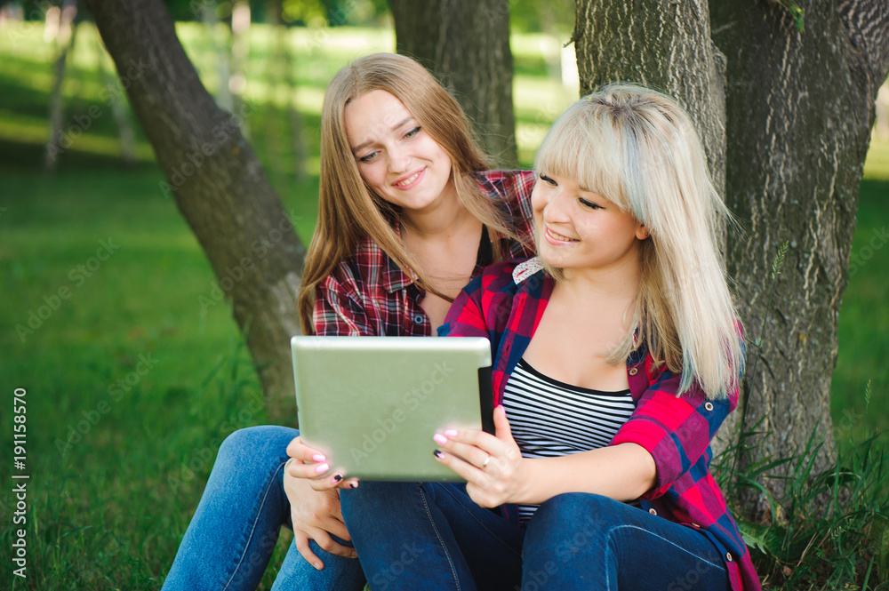 Obraz premium Smiling women using tablet ps on a green meadow