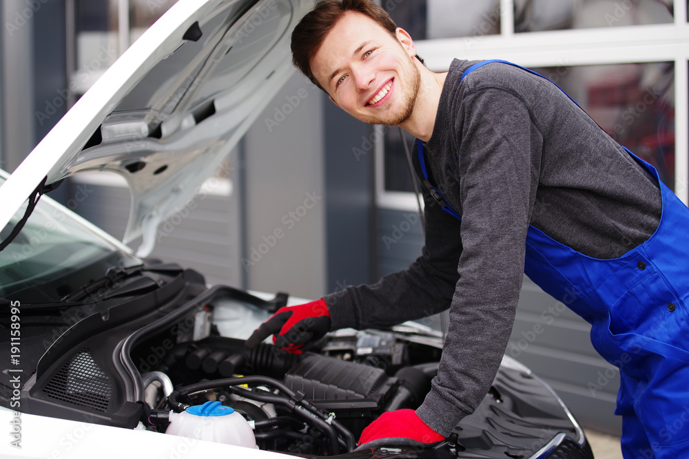 Automechaniker sympathisch lächelnd inspiziert einen Motor Automechaniker sympathisch lächelnd inspiziert einen Motor