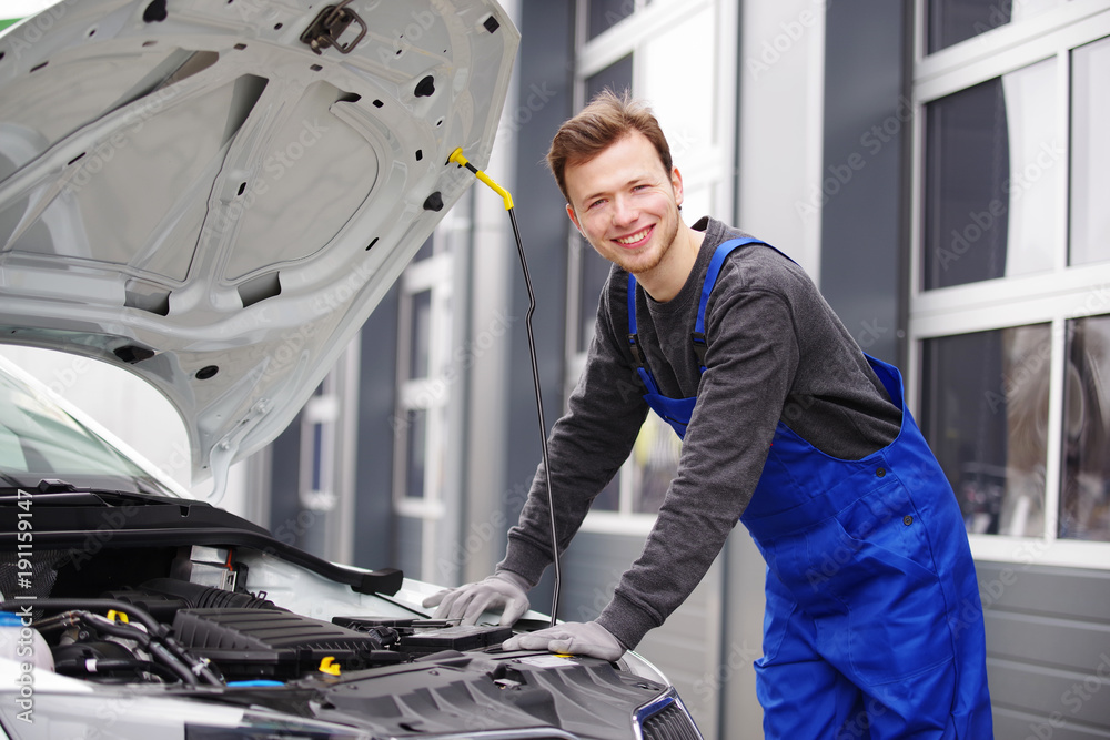 Automechaniker sympathisch lächelnd inspiziert einen Motor  - obrazy, fototapety, plakaty 