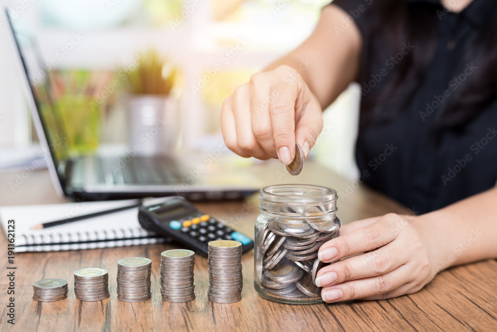 Saving money and finances concept, Close up hand woman hand put coins in jug glass with Calculate with a calculator.