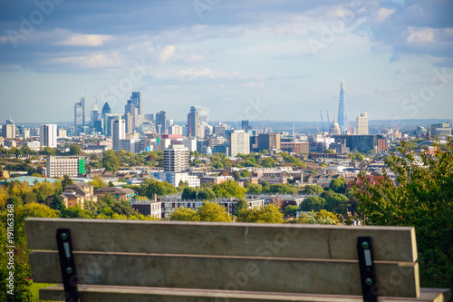 Photography View towards London city skyline from Hampstead Heath through an empty bench