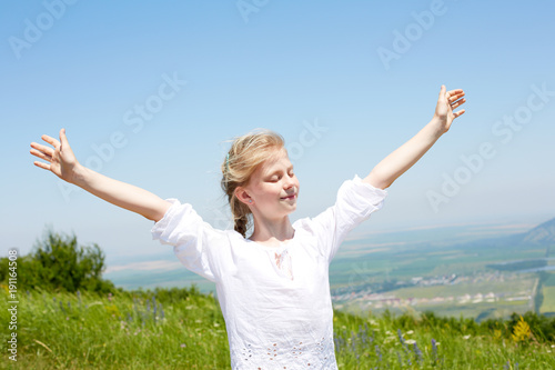 Concept of happiness. Cute happy child in white blouse on a rock with raised hands and looking to a valley below