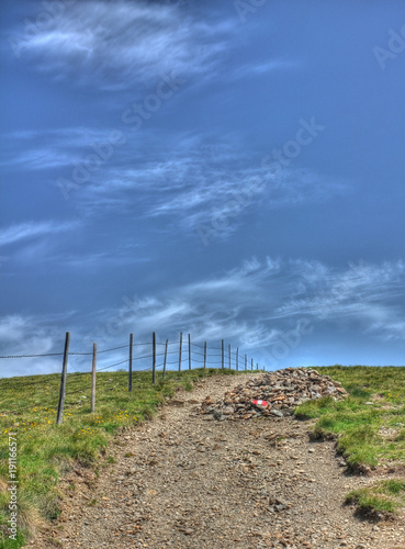Blue sky with some clouds over a rocky path along a wooden fence in Austrian mountains