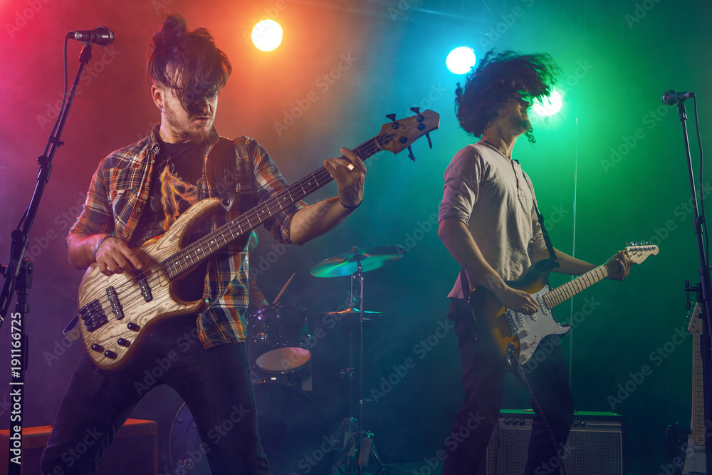 Obraz premium Rock band performs on stage. Guitarist, bass guitar and drums.