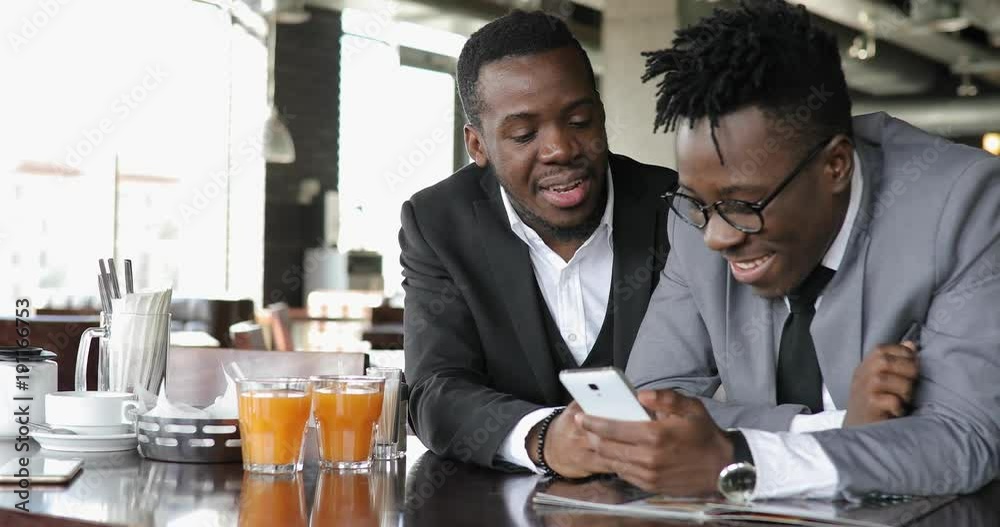 African businessmen friends watching funny photos together on smart phone in cafe African businessmen friends watching funny photos together on smart phone in cafe