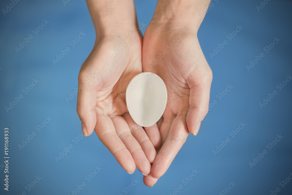 White eggshell in hands on a blue background White eggshell in hands on a blue background