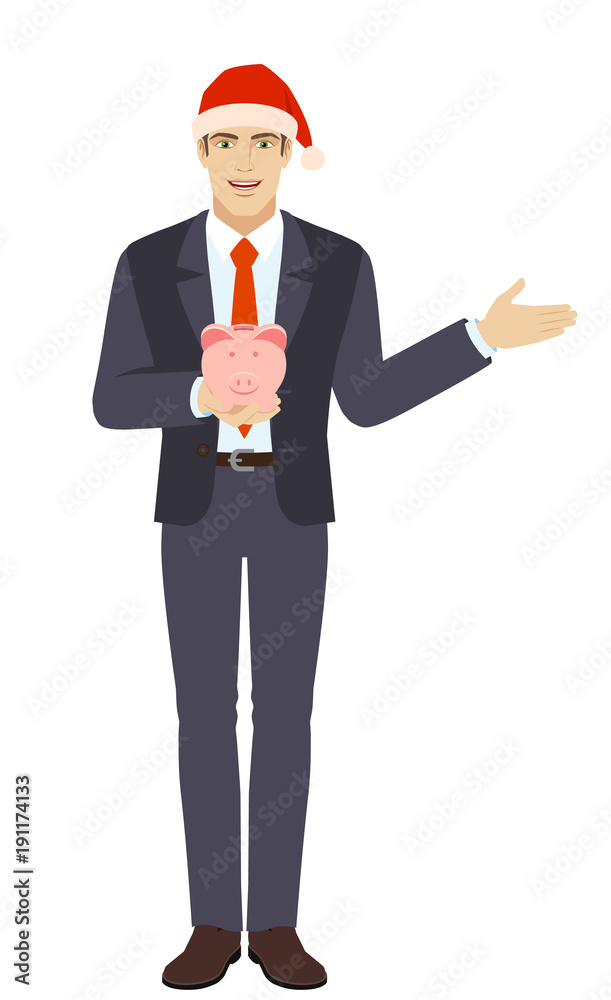 Businessman in Santa hat holding a piggy bank and showing something beside of him Businessman in Santa hat holding a piggy bank and showing something beside of him
