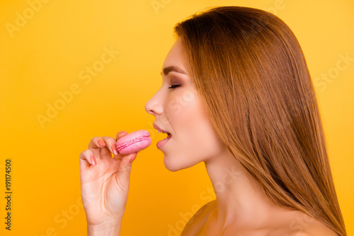 Close up profile of charming woman want to bite tasty pink macaron  holding macaroon near open mouth  beauty fashion girl enjoying food with close eyes  dieting concept  junk food  weight loss