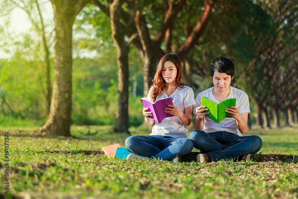 man and woman sitting and reading a book in park man and woman sitting and reading a book in park