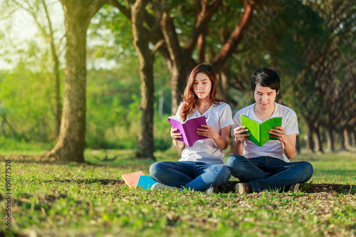 man and woman sitting and reading a book in park