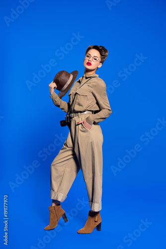stylish young woman in retro clothing with hat in hand isolated on blue