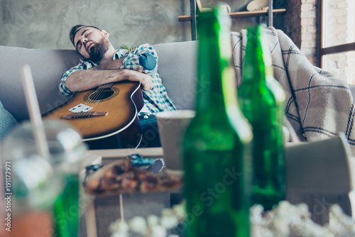 It was a great night! Drunk sleepy tired guy wearing checkered shirt is sleeping on a sofa and embracing an acoustic guitar