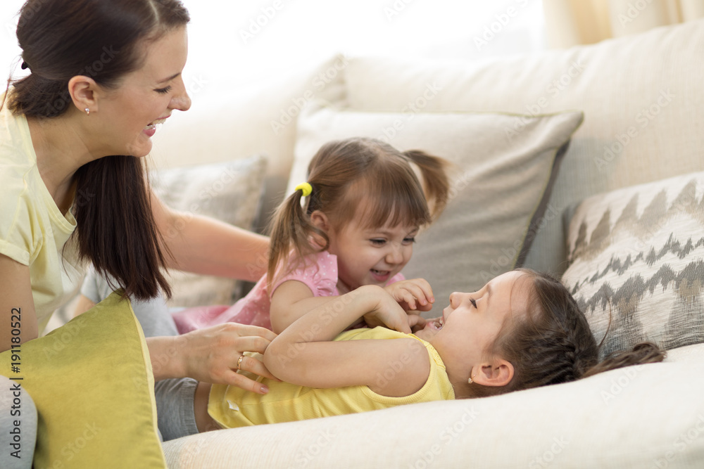 Smiling kids and their mom having a fun pastime together on couch in living room at home Smiling kids and their mom having a fun pastime together on couch in living room at home
