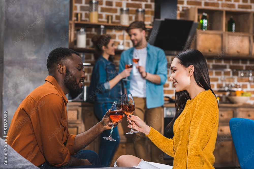 side view of young multiethnic couple drinking wine while friends standing behind