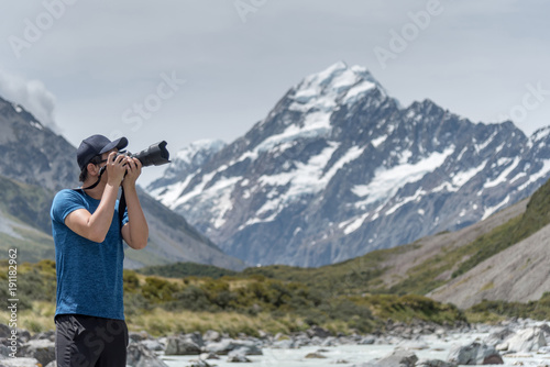 Young Asian male photographer taking photo at Mount Cook National Park in summer, Famous tourism spot of South Island, New Zealand