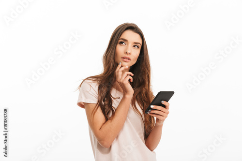 Pensive brunette woman in t-shirt holding smartphone and looking away