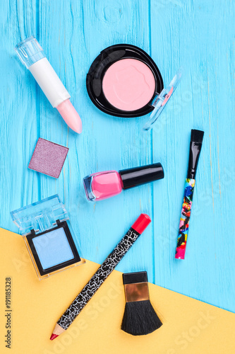 Set of cosmetics poducts, top view. Eyeshadows, blusher, lipstick, nailpolish, pencil, brushes on blue and yellow background. Cosmetics items for fashion makeup. photo