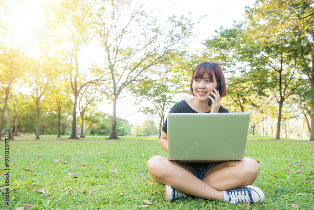 Cute asian woman smiles and talking on mobile phone while sitting in park spring day. Asian woman using on smart phone and laptop with feeling relax and smiley face. Lifestyle and technology concepts. Cute asian woman smiles and talking on mobile phone while sitting in park spring day. Asian woman using on smart phone and laptop with feeling relax and smiley face. Lifestyle and technology concepts.