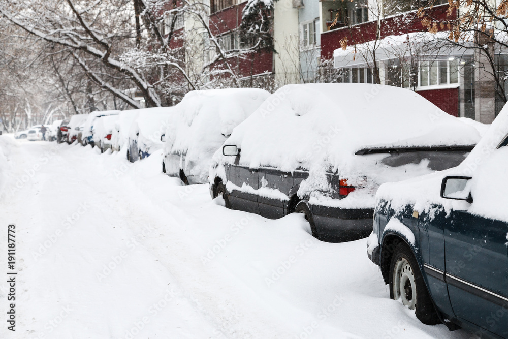 Snow covered cars on a parking near building