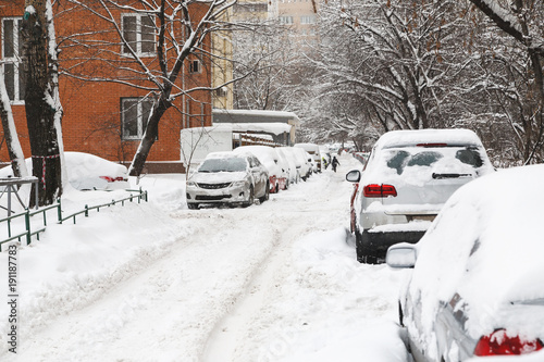 Snow covered cars on a parking near building