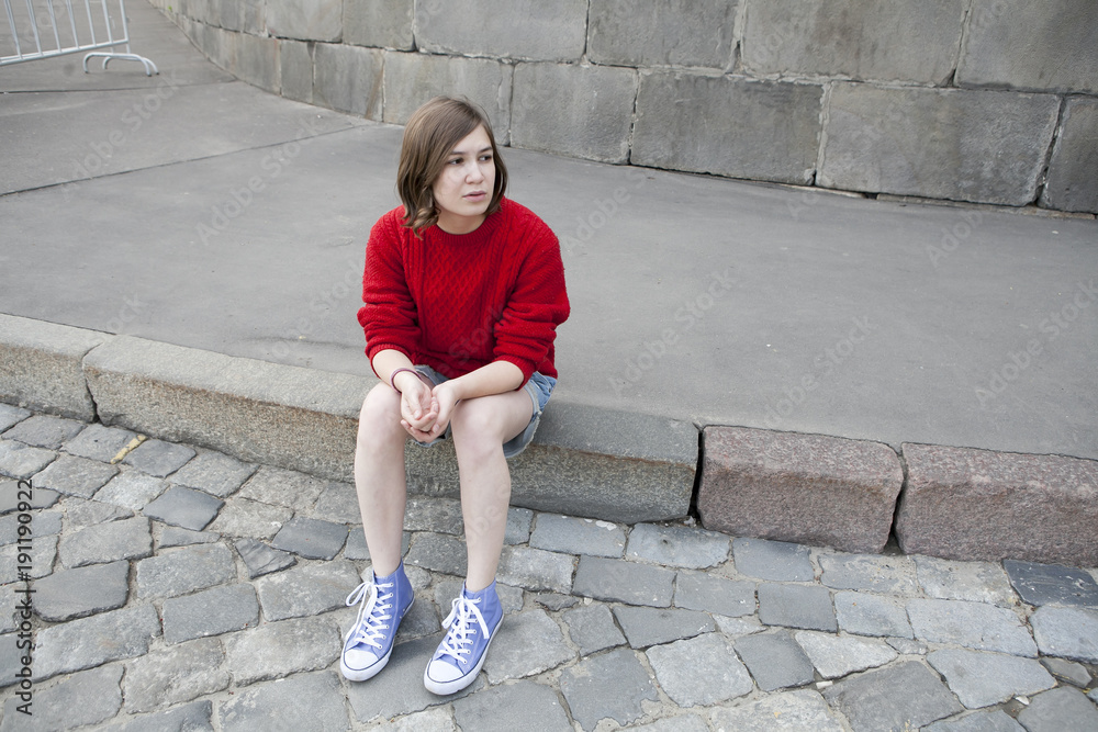young girl in a red wool sweater and jeans shorts is sitting on the steps young girl in a red wool sweater and jeans shorts is sitting on the steps