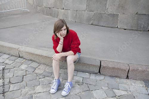 young girl in a red wool sweater and jeans shorts is sitting on the steps