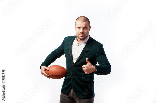 A young bald man in a white shirt, green suit holds a rugby ball poses on a white isolated background