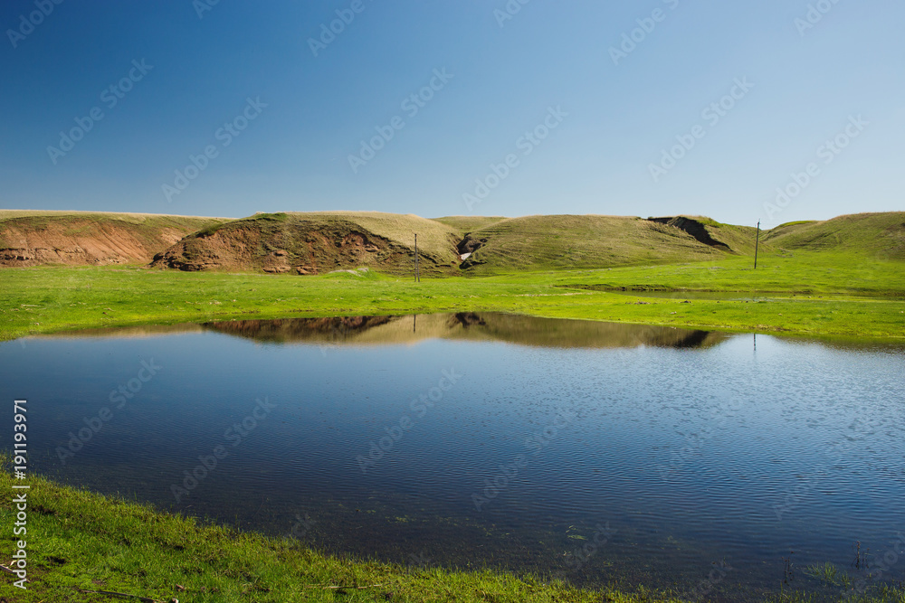 small lake on the background of blue sky and green fields.