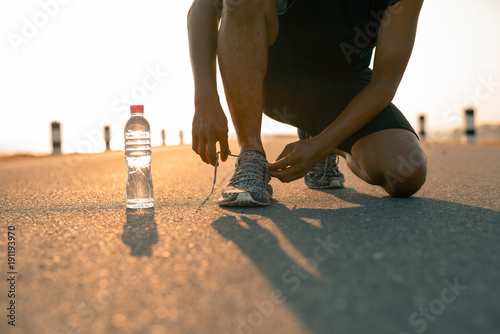Male runner tying shoes in preparation for a run in the morning and bottle water. The concept of health and fitness