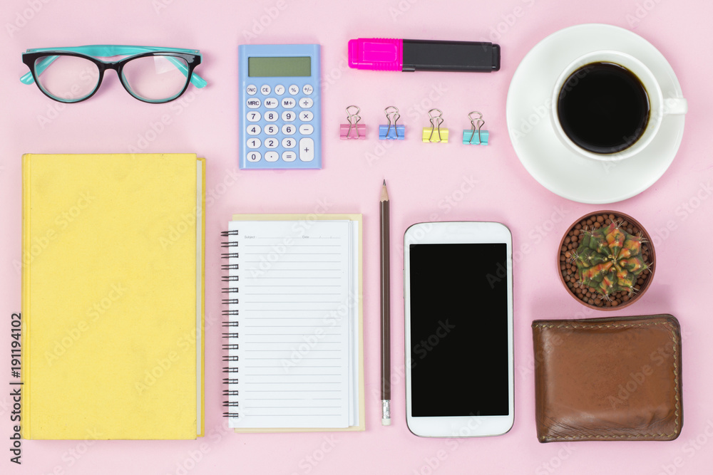 Mobile and old book and notebook pencil glasses black coffee white cup and paper clip cactus on pink background flatlay pastel style.