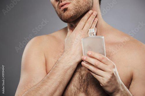 Tableau sur toile Portrait cropped of handsome half-naked man putting perfume on his neck, isolate