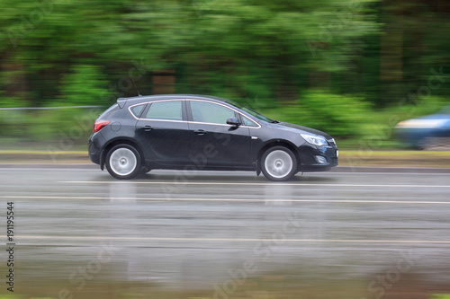 Black car is driving on a wet road. Urban life. © tikhomirovsergey