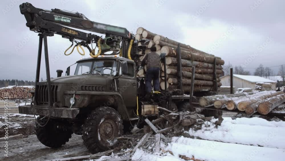 Workers climbs on lorry truck crane on dirty road at woodwork production yard, winter cloudy day Workers climbs on lorry truck crane on dirty road at woodwork production yard, winter cloudy day