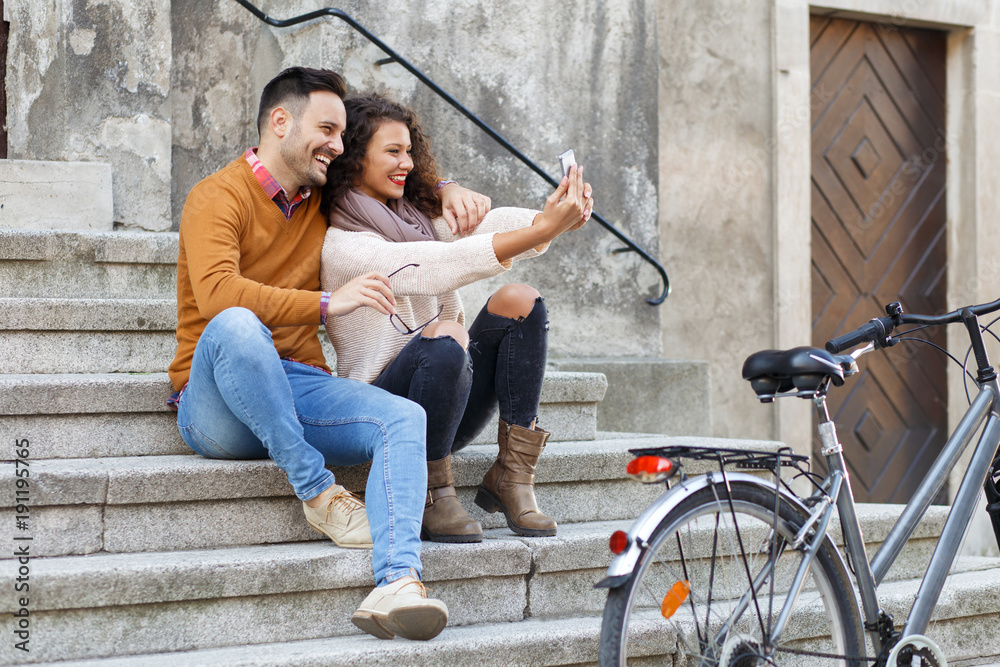 Young smiling couple using mobile phone while sitting on the stairs.