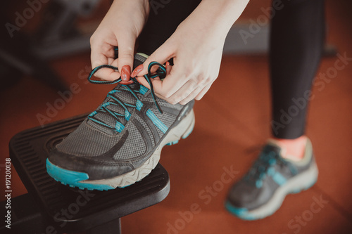 Close-up of girl tying shoelaces on sports shoes in gym.
