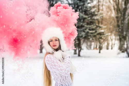 Young caucasian female in sweater with red smoke bomb on snow winter day